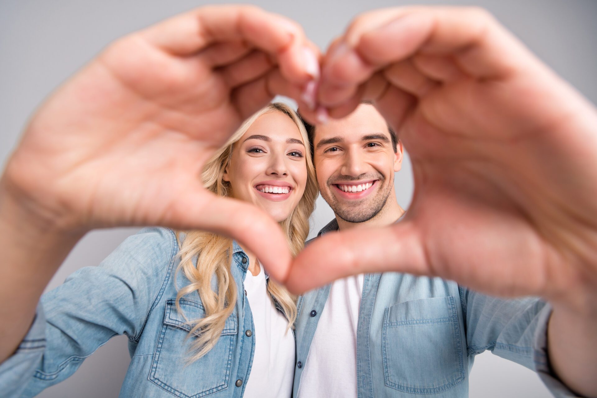 Photo of young couple happy positive smile show fingers heart figure love romantic isolated over grey color background Photo of young couple happy positive smile show fingers heart figure love romantic isolated over grey color background.